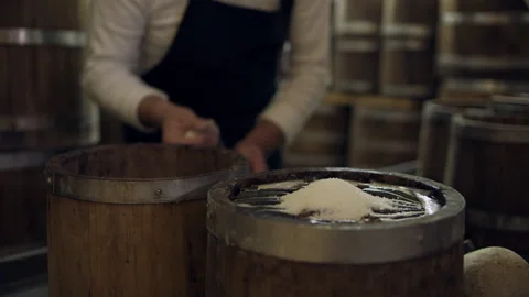 In a cellar with barrels, a focused older man puts salt on a layer of anchovies Stock Footage 199458979