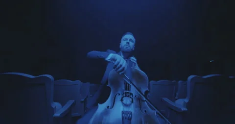 A cellist performs in an empty hall, immersed in mysterious blue light. Stock Footage 303390326