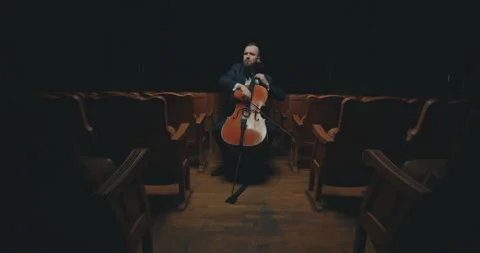 A cellist plays classical music in an empty, dark hall of an ancient theater. Stock Footage 303390221