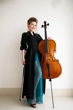 Cellist posing while standing with a cello against a light wall Stock Photos