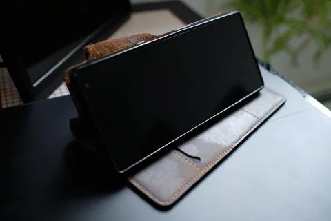 A cellphone in a brown leather case is stood up on top of a black lap top on  Stock Photos
