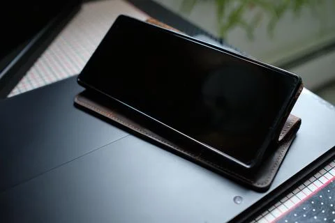 A cellphone in a brown leather case is stood up on top of a black lap top on  Stock Photos