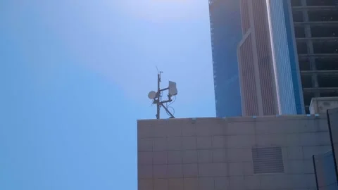 Cellular antennas are positioned high on corner of a building against a blue sky Video stock 333325818
