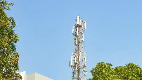 Cellular communication tower against the backdrop of the sky and trees Stock Photos