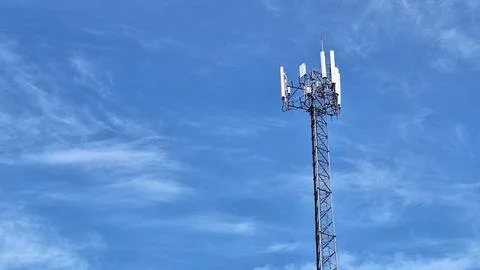 Cellular Communication Tower Against Blue Sky with Wispy Clouds and Modern .. Stock Photos