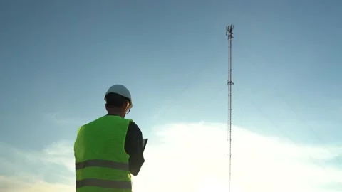 Cellular engineer in a helmet with a tablet and a phone next to the mast Stock Footage 156465949