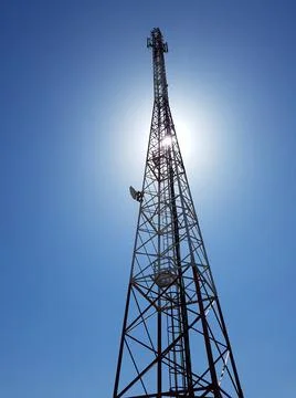 Cellular or mobile network tower against the sun in the blue sky. Stock Photos