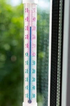 A Celsius thermometer on a window frame shows high temperatures of 34 degrees Stock Photos