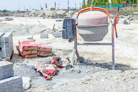 Cement mixer machine is at construction site with cement bags and curbstone.. Stock Photos