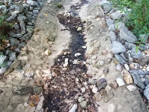 Cement or concrete gutter with rocks or stones with mud Stock Photos