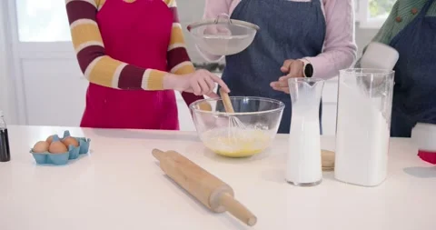 Center hands are whisking eggs at counter as hand is sifting flour into bowl Video stock 345270738