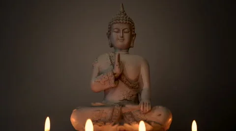 Centered meditating Buddha statue lit by candle light against dark background Stock Footage 65489081