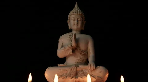 Centered sitting Buddha statue lit by candle light against black background Stock Footage 65489340