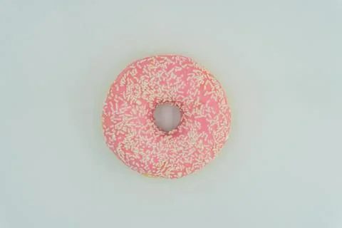 A centered, slightly angled doughnut with pink glaze and sprinkles on a light Stock Photos