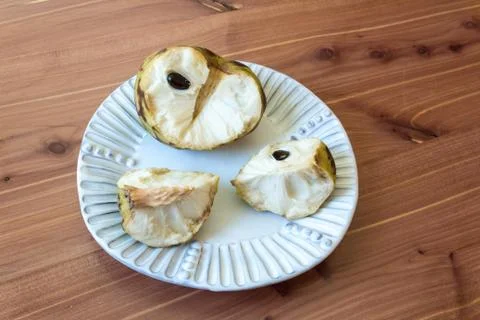 Centered white plate with one half and two quarters of a ripe cherimoya fruit Stock Photos
