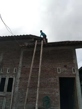 CENTRAL JAVA, INDONESIA - OCT 30, 2026: A brave man climbs a high roof using a t Stock-Fotos