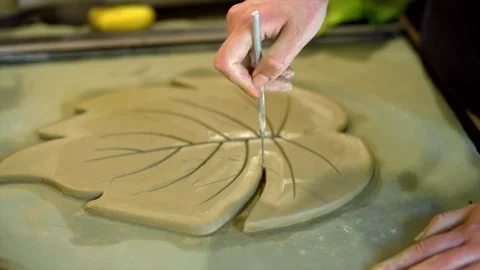 Ceramic artist carving monstera leaf patterns in wet clay using needle tool. Stock Footage 339258783