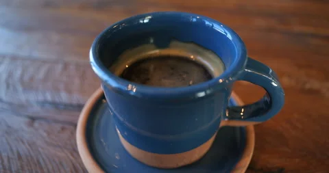 A ceramic blue cup with black coffee on a blue saucer stands on a wooden table Stock Footage 232299313