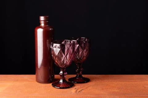 Ceramic bottle of wine and two red faceted glasses on a wooden table. 写真素材