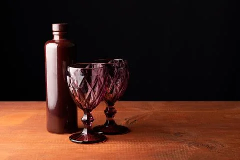 Ceramic bottle of wine and two red faceted glasses on a wooden table. Stock Photos