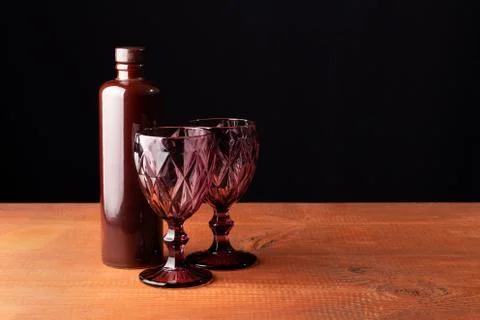 Ceramic bottle of wine and two red faceted glasses on a wooden table. Stock Photos