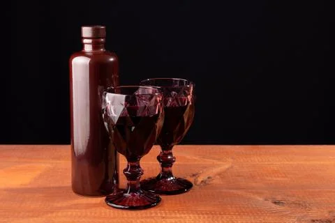 Ceramic bottle of wine and two red faceted glasses on a wooden table. 写真素材