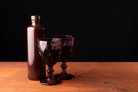 Ceramic bottle of wine and two red faceted glasses on a wooden table. Stock Photos