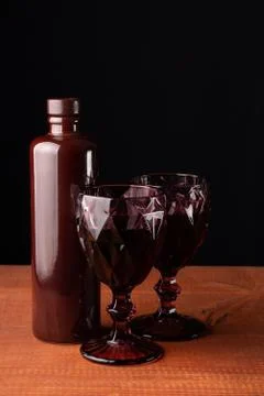 Ceramic bottle of wine and two red faceted glasses on a wooden table. 写真素材