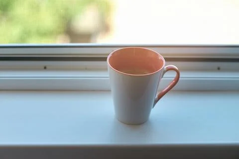 A ceramic coffee mug sitting on a white windowsill near a window Stock Photos