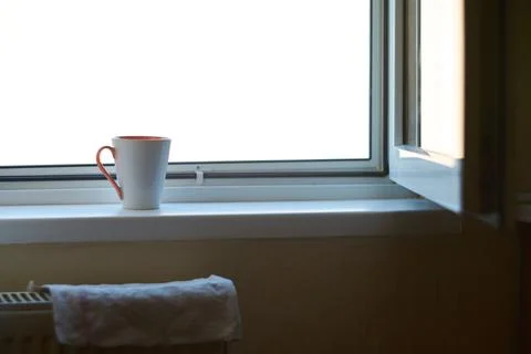 A ceramic coffee mug sitting on a windowsill next to an open window Stock Photos