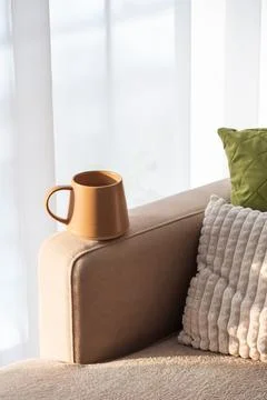 Ceramic Coffee Mug on Sofa Armrest with Textured Pillows. Cozy Home Interior Stock Photos