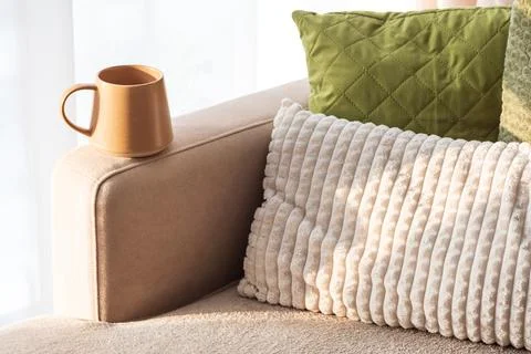 Ceramic Coffee Mug on Sofa Armrest with Textured Pillows. Cozy Home Interior Stock Photos