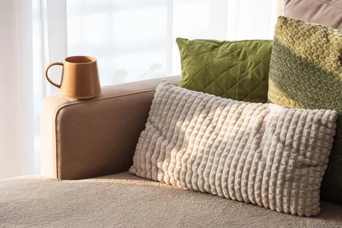Ceramic Coffee Mug on Sofa Armrest with Textured Pillows. Cozy Home Interior Stock-Fotos