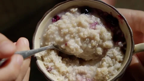 Ceramic cup being gently held, creamy oatmeal presenting fresh berries in soft Video stock 308680077