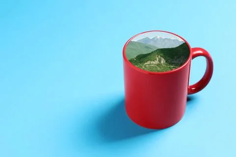Ceramic cup with mountain landscape instead of drink on light blue backgrou.. Stock-Fotos