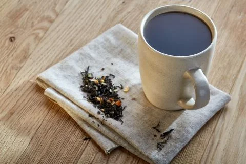Ceramic cup of tea with scattered tea leaves on a napkin on rustic wooden Stock Photos