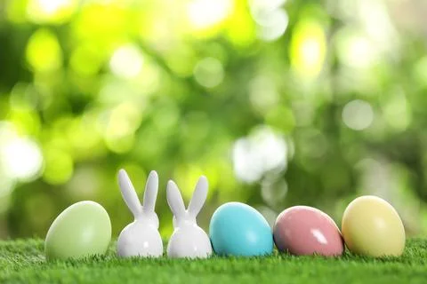 Ceramic Easter bunnies and dyed eggs on green grass against blurred backgroun Foto stock
