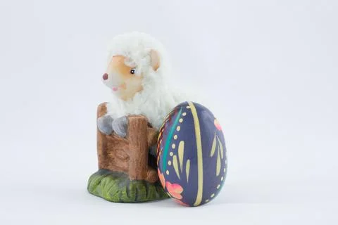 Ceramic figurine of an Easter lamb with an egg next to it on a white backgrou Stock Photos