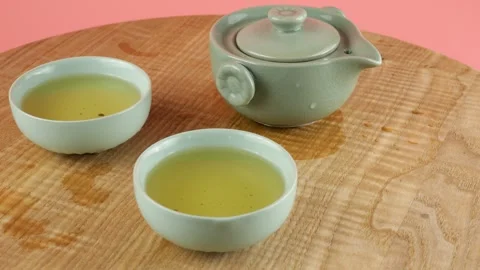 Ceramic gaiwan and two chawans of green tea rotate on a wooden board.  動画素材 287248334