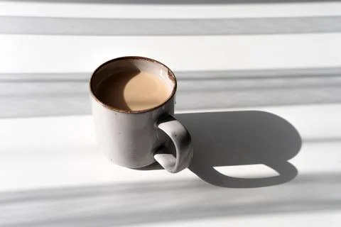 Ceramic Mug of Coffee or Tea Casting a Strong Shadow on a White Surface Foto stock