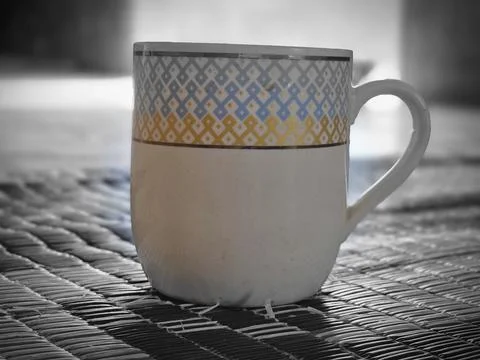 Ceramic mug with decorative pattern placed on a traditional black woven mat. Stock Photos