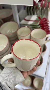 Ceramic mug with red rim held in hand among similar mugs on display Foto stock