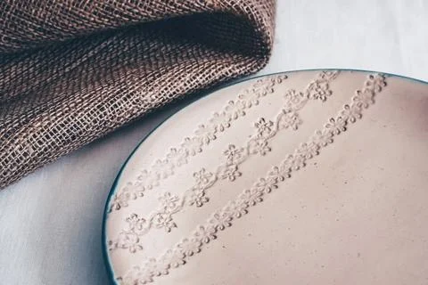 Ceramic plate with embossed floral pattern on linen tablecloth with burlap Stock Photos