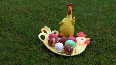 Ceramic rooster near dyed easter eggs on the chicken-shaped plate on green Stock Footage 267278600
