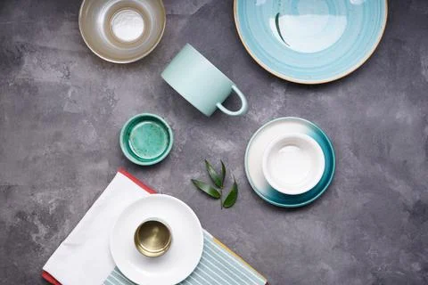 Ceramic small tableware and kitchen towel on gray background, top view. Stock Photos