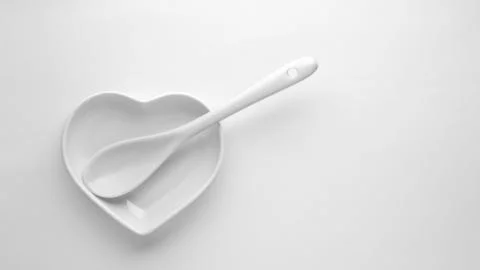 Ceramic spoon and an empty plate in the shape of a heart on a white backgroun Stock Photos