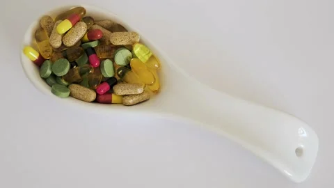 Ceramic spoon with colored pills, dietary supplements on a white background. The Stock Footage 233008491