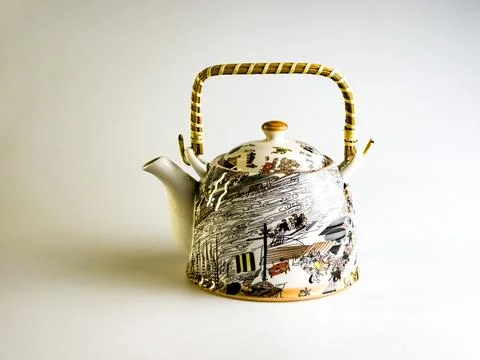 Ceramic teapot with abstract pattern and wicker straw handle on a white backg Stock Photos