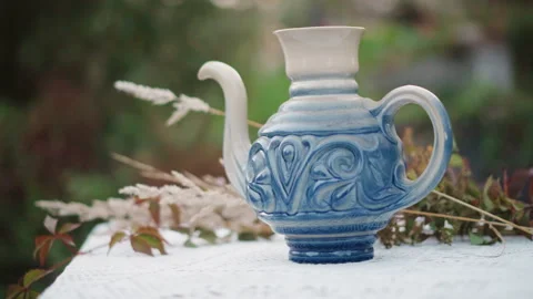 Ceramic teapot setting. Cozy garden tea display with blurred background figures Stock Footage 346390837