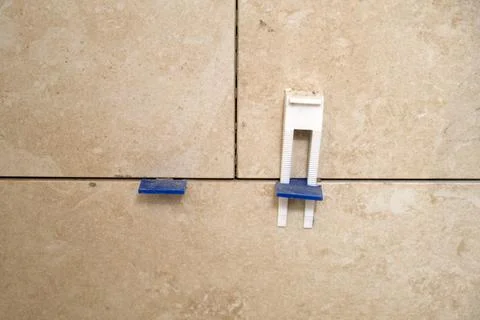 Ceramic tile being installed on wall with leveling system spacer and wedge. R Stock Photos